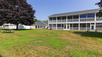 A two-story building with balconies, a grassy lawn, and a tree.