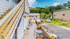 A wooden deck with outdoor seating, a covered area, and a view of a residential area with houses and a car. - Shorelands, Unit 44-3  | Condo in Kennebunk with pool and playground access (Kennebunk)