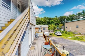 A wooden deck with outdoor seating, a covered area, and a view of a residential area with houses and a car. - Shorelands, Unit 44-3  | Condo in Kennebunk with pool and playground access (Kennebunk)