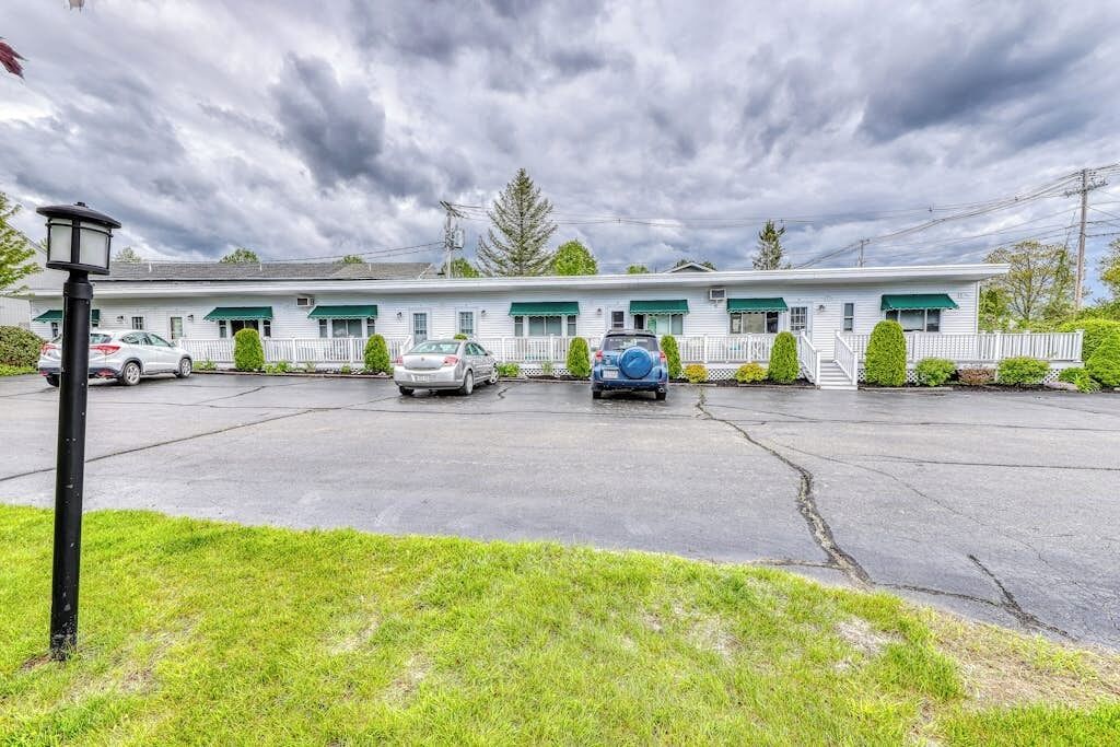 A motel with a row of rooms, a parking lot, and a grassy area in front.