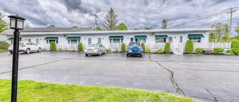 A motel with a row of rooms, a parking lot, and a grassy area in front.