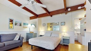 Une chambre à coucher comprenant un lit, un canapé, un plancher en bois, un ventilateur de plafond et des lampes fixées au mur.