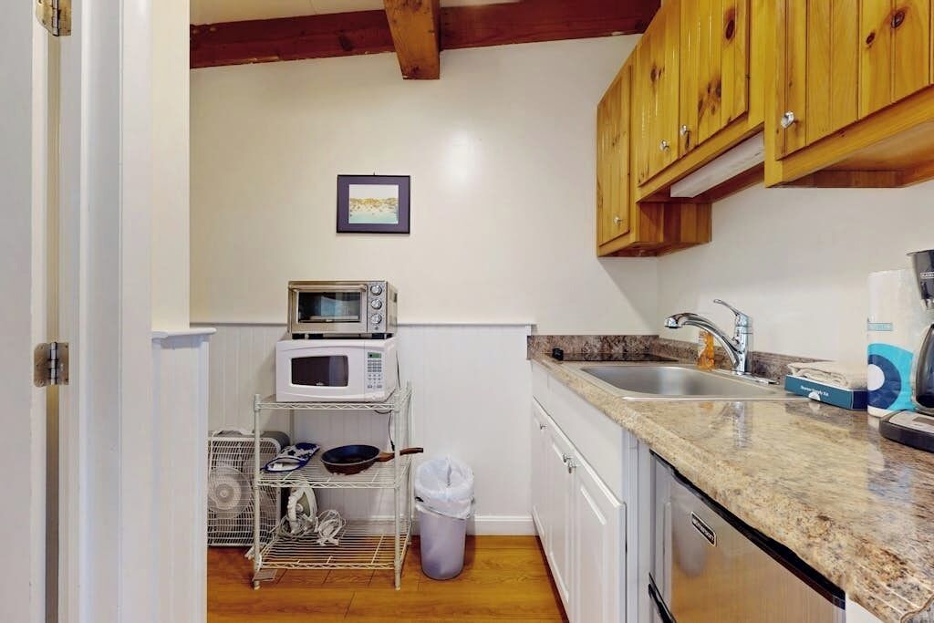 A kitchen with white cabinets, a microwave, a sink, and a dish rack.