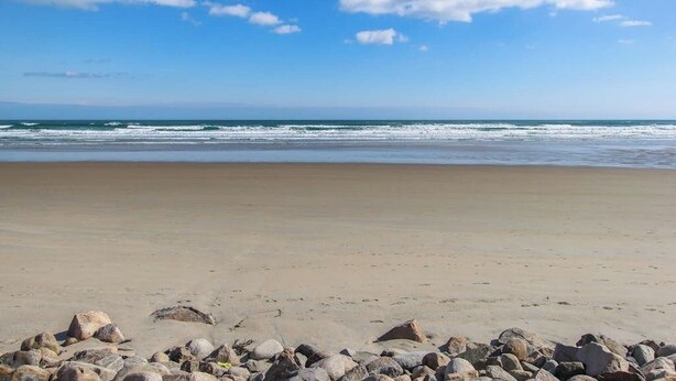 Une plage avec un ciel dégagé, des vagues et des rochers éparpillés.