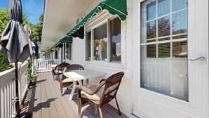 Une terrasse couverte, aménagée avec du mobilier d’extérieur, dotée d’une rambarde blanche et surmontée d’une marquise verte.