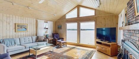 A spacious living room with a large TV, wooden walls, a sofa, and a fireplace.