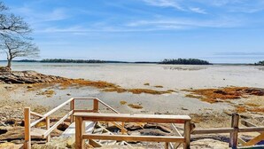 Eine Holzterrasse führt zu einem Strand, der unter blauem Himmel liegt.