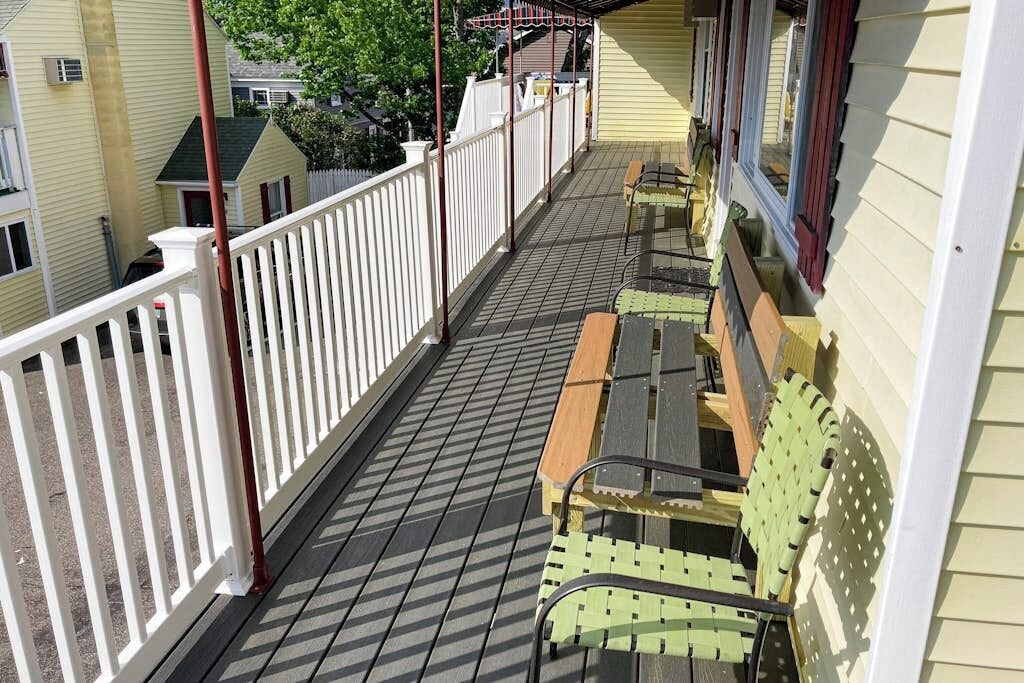 En balkon med et træbord og stole, et hvidt gelænder og udsigt til nabohuse.
