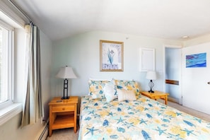 A bedroom with a bed, two bedside tables, a window with curtains, and a door. - Ocean-view condo with gorgeous sunrises, deck, & WiFi - walk to beach & pier (Old Orchard Beach)