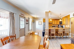 A dining area with a wooden table and chairs, a kitchen with wooden cabinets, and a window with curtains. - Ocean-view condo with gorgeous sunrises, deck, & WiFi - walk to beach & pier (Old Orchard Beach)