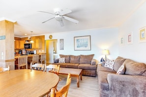 A living room with a sofa, a dining table, and chairs. There is a kitchen area with cabinets and a refrigerator. - Ocean-view condo with gorgeous sunrises, deck, & WiFi - walk to beach & pier (Old Orchard Beach)