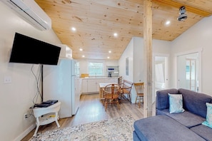 Un intérieur moderne avec un téléviseur à écran plat, un coin repas comprenant une table et des chaises en bois, un canapé gris et un tapis à motifs.