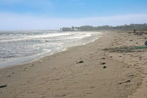 Ein Strand mit sandigem Ufer, vereinzelten Felsen und einer fernen Küstenlinie mit Gebäuden.