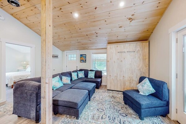 Ein modernes Wohnzimmer mit Holzboden, einem Ecksofa, Poufs und einem gemusterten Teppich.