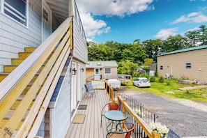 Une terrasse en bois avec des sièges extérieurs, un espace abrité et une vue sur un quartier résidentiel.