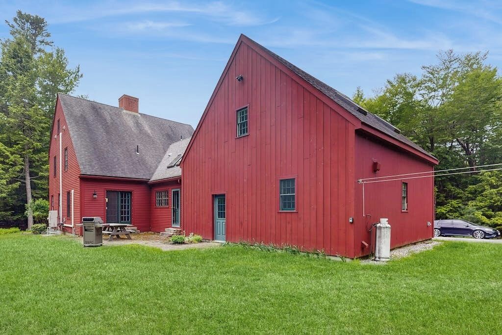 A red barn with a sloped roof, a picnic table, and a car parked nearby.