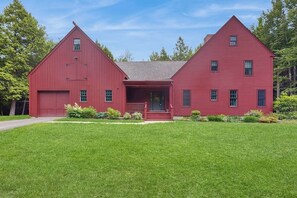 A red two-story house with a front porch, a garage, and a well-maintained lawn. - Spacious retreat with peaceful seclusion, Wifi, Patio & BBQ Grill (Freeport)