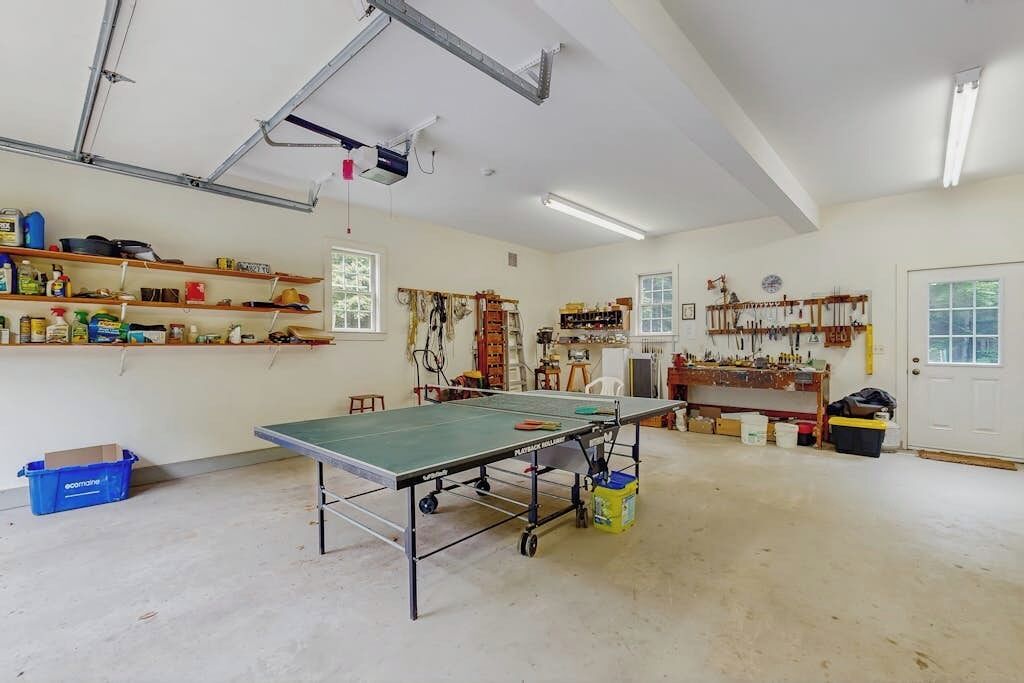 Een ruime kamer met een tafeltennistafel, planken met verschillende spullen, en een deur.
