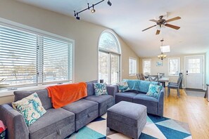 A spacious living area with a gray sectional sofa, ottoman, and a dining table with chairs.