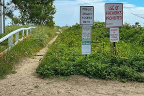 A pathway leading to a beach with signs indicating public beach access, no use of fireworks, and warnings about nesting piping plovers. - Serene Coastal Retreat with Breathtaking Ocean Views and Fire pit (Biddeford)