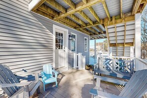 A covered porch with wooden beams, a door, and two blue Adirondack chairs. - Serene Coastal Retreat with Breathtaking Ocean Views and Fire pit (Biddeford)