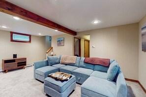 A living room with a sectional sofa, a wooden entertainment unit, and a ceiling with exposed beams.