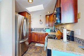 A modern kitchen with wooden cabinets, a stainless steel refrigerator, granite countertops, and a skylight.