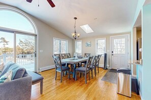 A dining area with a table and chairs, a ceiling fan, a chandelier, and a view through large windows.