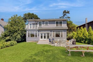 Ein zweistöckiges Haus mit Veranda, überdachter Terrasse und Garten mit Picknicktisch.