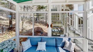 Ein Wintergarten mit blauer Couch, gemusterten Kissen und Blick auf ein bewaldetes Gebiet.