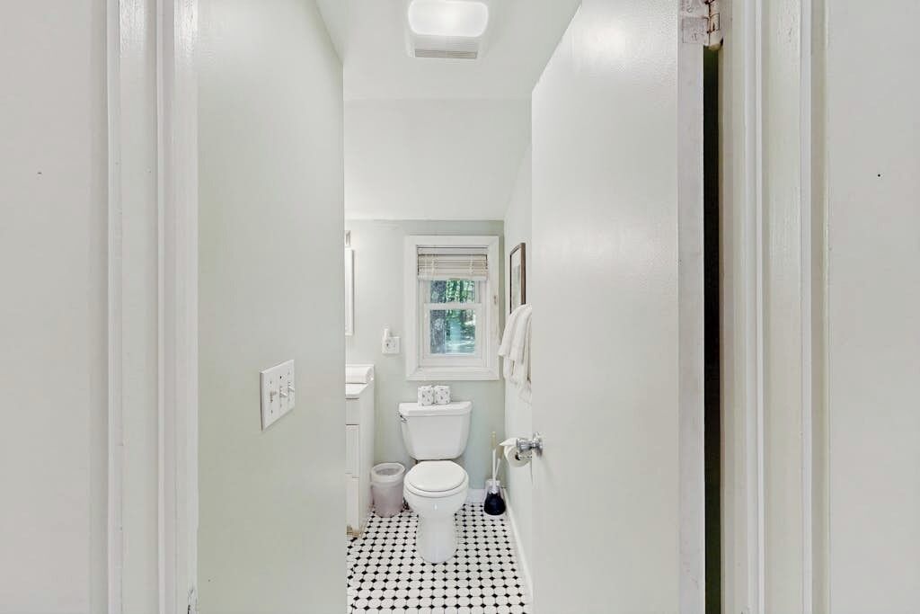 A narrow hallway leading to a small bathroom with a toilet, a sink, and a window.