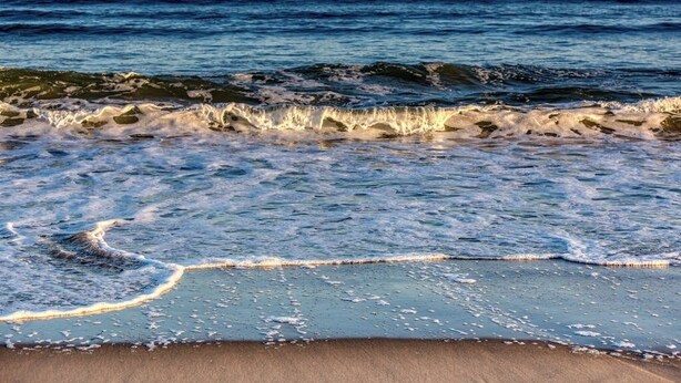 Una playa con olas, cielo despejado y mar tranquilo.