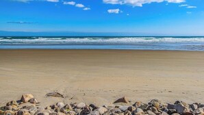 A beach with a clear sky, waves, and scattered rocks. - Charming condo with pool and deck space (Wells)
