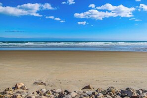 A beach with a clear sky, waves, and scattered rocks.