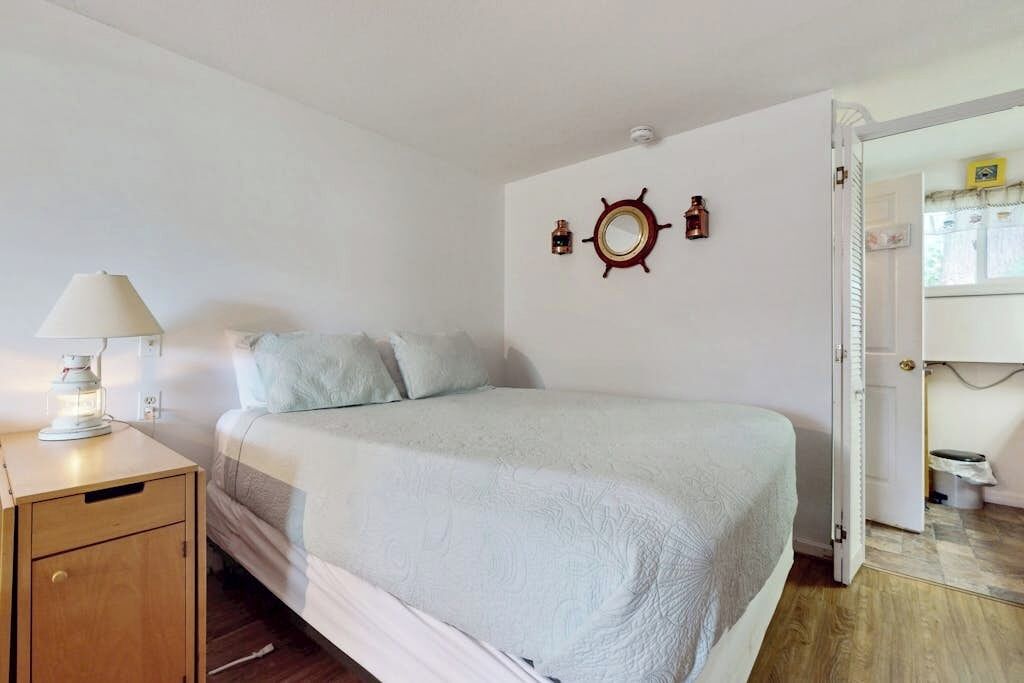 A bedroom with a bed, a nightstand with a lamp, a wooden cabinet, and a door leading to another room.
