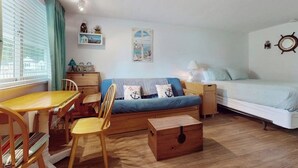 A compact room with a bed, a sofa, a dining table with chairs, a small cabinet, and a wooden chest. - Charming condo with pool and deck space (Wells)
