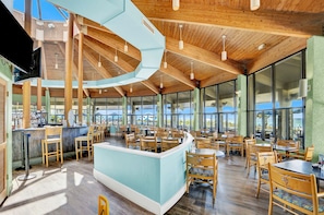 Ein geräumiges Restaurant mit hoher Decke, Holzbalken und großen Fenstern mit Blick.