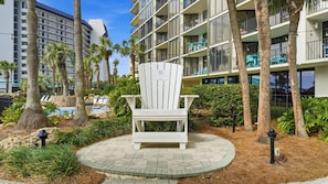 Ein weißer Adirondack-Sessel in einer angelegten Grünanlage mit Pool, Palmen und einem Gebäude mit Balkonen.