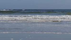 Een strand met golven, heldere lucht en een kalme zee.
