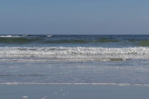 Ein Strand mit Wellen, blauem Himmel und ruhiger See.