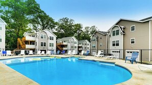 A swimming pool with lounge chairs, a wooden deck, and residential buildings with balconies. - Cheerful condo one mile from Ogunquit Beach with a pool - near dining (Wells)