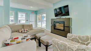 A living room with a sofa, ottoman, patterned armchair, fireplace, and a television mounted on the wall. - Cheerful condo one mile from Ogunquit Beach with a pool - near dining (Wells)