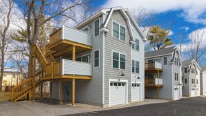 A two-story residential building with a wooden deck, a garage, and a second-story balcony. - Cheerful condo one mile from Ogunquit Beach with a pool - near dining (Wells)