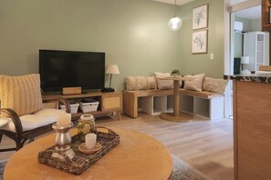 Uma sala de estar com televisão, sofá, mesa de centro e um pequeno espaço de jantar.