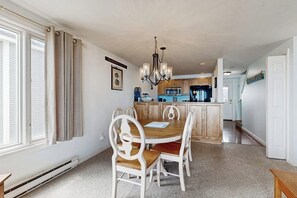 Ein Essbereich mit einem runden Tisch, weißen Stühlen, einer Chandelierleuchtre und einer Küche im Hintergrund.