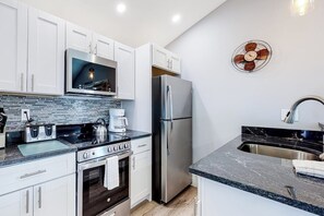 A modern kitchen with white cabinets, a stainless steel refrigerator, a microwave, and a coffee maker.