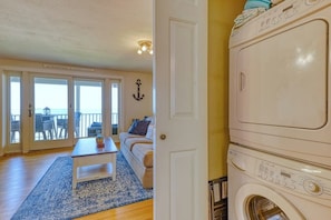 A room with a washing machine, a sofa, a coffee table, and a view through a glass door.