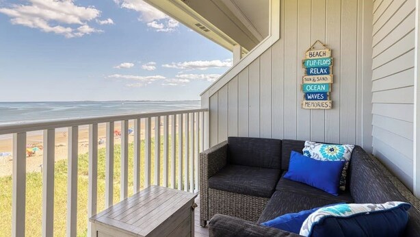 Ein Balkon mit Blick auf den Strand, ein Korbssessel mit blauen Kissen und ein Holztisch.