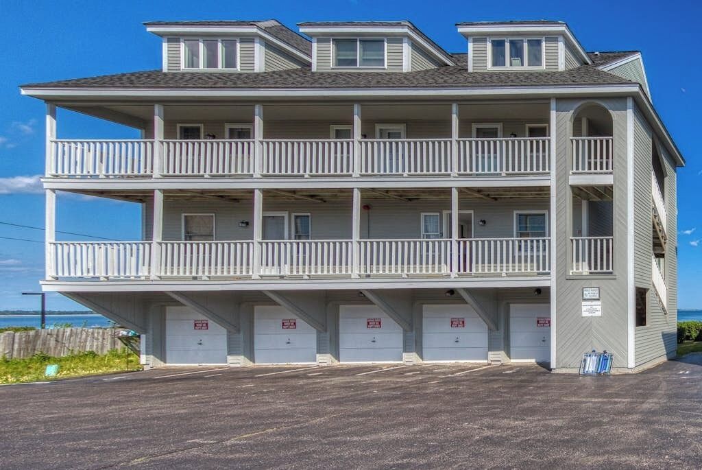 A multi-story building with balconies, a parking area, and a view of the ocean.