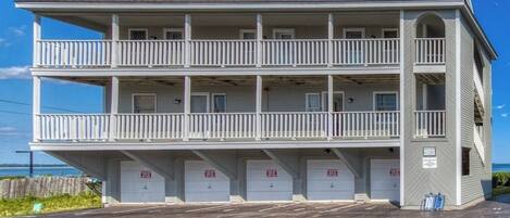 A multi-story building with balconies, a parking area, and a view of the ocean.